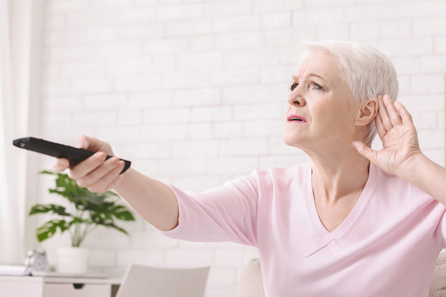 woman with difficulty hearing television cupping ear and holding remote control