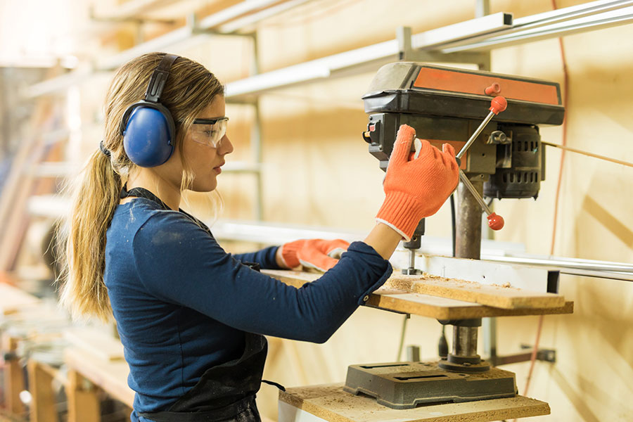 woman using drill press wearing noise cancelling earmuffs