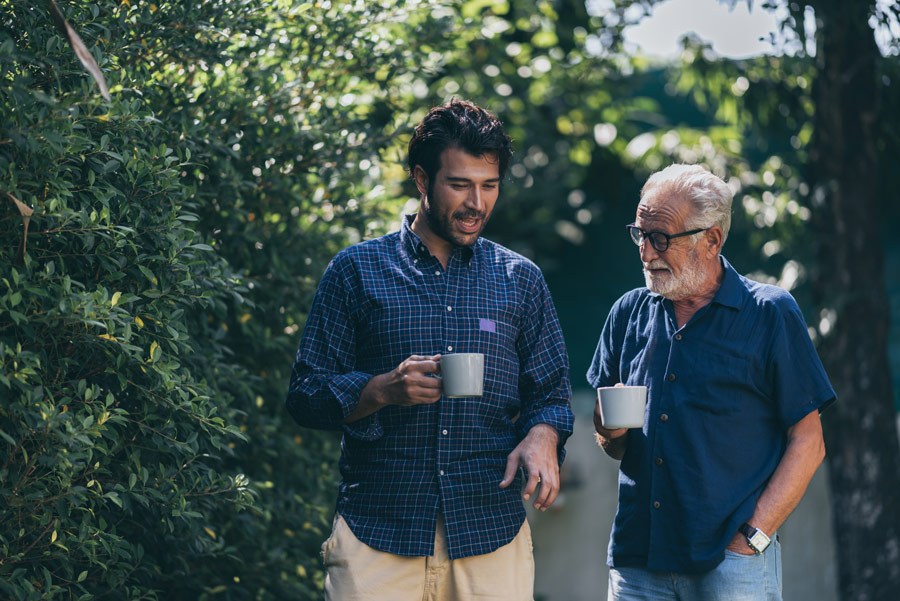 featured image for article on hearing and cognitive function showing father and adult son walking and drinking coffee outside