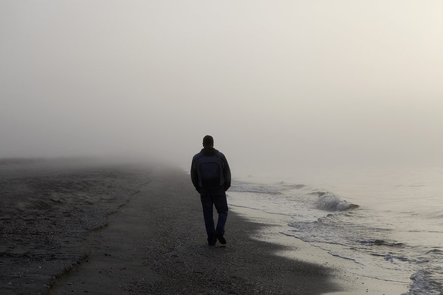 man walking alone on beach shrouded in fog