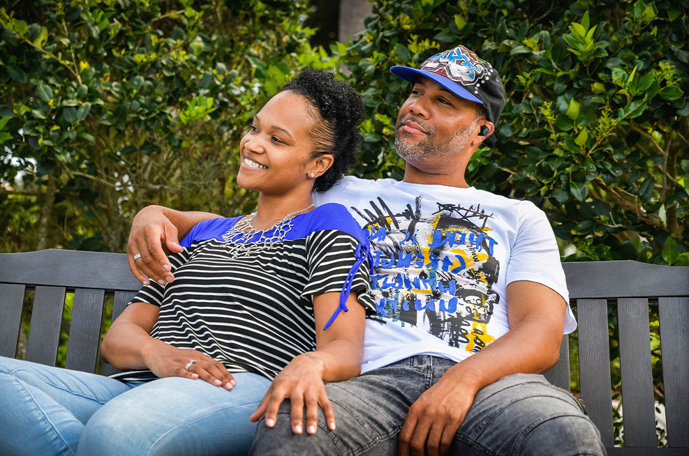 man wearing hearing enhancement earphones, sitting with partner on bench